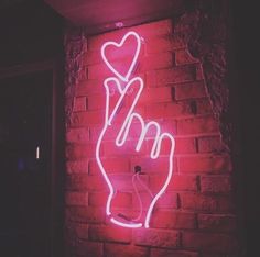 a neon sign that is on the side of a brick wall with a hand holding a heart