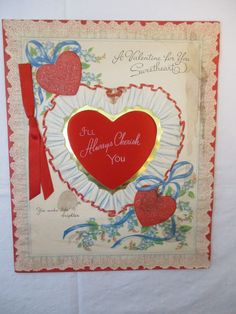 a valentine's day card with a heart and ribbon on the front, attached to a wall