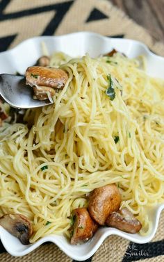 a white bowl filled with pasta and mushrooms on top of a tablecloth next to a spoon