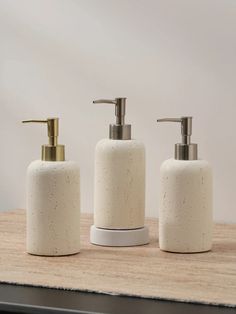 three white soap dispensers sitting on top of a wooden table