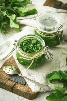 two jars filled with green pestle sitting on top of a cutting board next to a spoon