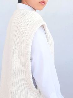 a woman wearing a white sweater vest and black hair is looking off to the side