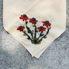 red flowers are embroidered onto a white handkerchief on the ground, with green stems sticking out of it