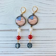 Show your patriotic love this 4th of July with these festive American flag earrings created by using the decoupage technique of adhering an American Flag print under a glass lens and then mounting it in a brass cup in an antique bronze finish. Dangling red, white and blue glass beads complete the earring with a total drop length of 3-Inches. A show-stopping set of patriotic earrings perfect to complete your red and white and blue style on Memorial Day, 4th of July, Veteran's Day, Flag Day or any Flag Earrings, Proud To Be An American, Patriotic Earrings, American Flag Print, Army Wife, Lightweight Earrings, Blue Style, Light Weight Earrings, Proud To Be