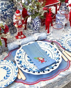 a table set with blue and white plates, napkins, silverware and red flowers