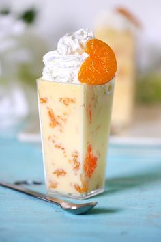 an orange dessert with whipped cream in a glass on a blue table cloth next to a fork