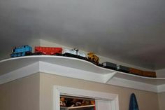 a toy train set on top of a shelf above a door in a room with gray walls