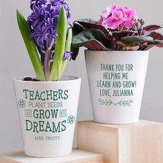 two flower pots with flowers in them sitting on top of a wooden block next to each other