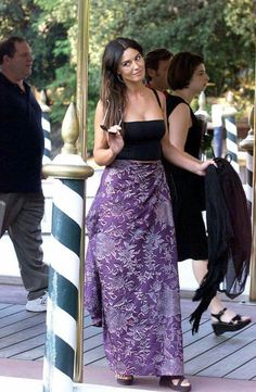 a woman in a long purple dress is standing on the sidewalk and talking to someone