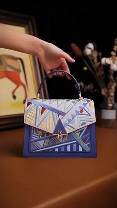 a woman's hand is holding a small blue and white purse with geometric designs on it