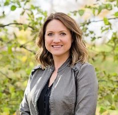 a woman standing in front of trees with her arms crossed and smiling at the camera