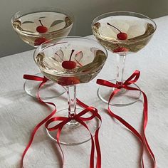 three martini glasses with cherries in them on a white tablecloth and red ribbon