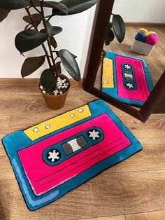 a pink and blue rug with an old school cassette tape design on the floor next to a potted plant