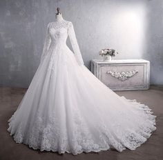 a white wedding gown with long sleeves and lace on the skirt, in front of a dresser