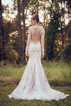 a woman in a wedding dress standing in the grass with her back to the camera