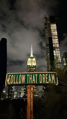 a green street sign sitting in front of a tall building with a sky filled with clouds