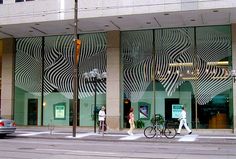 two people crossing the street in front of a building with zebra stripes on it's windows