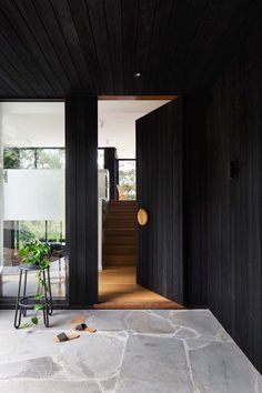 an open door leading into a black house with wood paneling and stone flooring