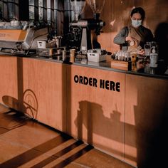 a woman wearing a face mask behind a counter with coffee cups and other items on it