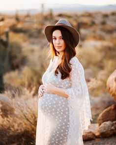 a pregnant woman wearing a white dress and hat poses for a photo in the desert