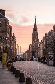 a cobblestone street with people walking on the sidewalk and buildings in the background