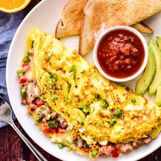 an omelet on a plate with fruit, bread and salsa next to it