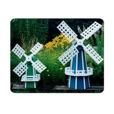 two wooden windmills sitting next to each other in front of some trees and flowers