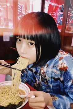 a woman eating noodles with chopsticks at a table