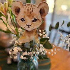 a small stuffed animal sitting on top of a glass vase filled with flowers and greenery