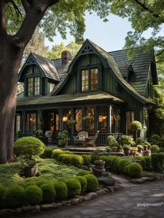 a green house with lots of trees and bushes in the front yard, surrounded by stone pavers