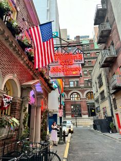 a woman standing in front of a building with an american flag hanging from it's side