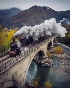 a train traveling over a bridge with steam pouring out of it