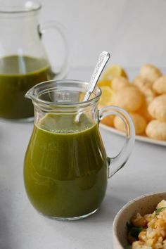 a pitcher of green liquid next to a bowl of food on a white tablecloth