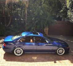 a blue car parked in front of a house on a brick driveway next to trees