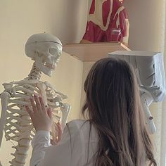 a woman standing in front of a mirror looking at a skeleton on top of a shelf