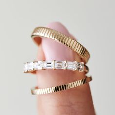 a woman's hand holding three gold rings with white stones on each side and one diamond in the middle