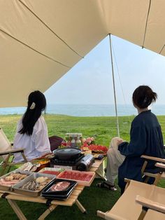 two people sitting in chairs under a tent with food on the table next to them