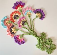 crocheted flowers are arranged on a white surface with green stems in the center