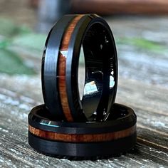 two black ceramic rings with wood inlays on top of each other sitting on a wooden table