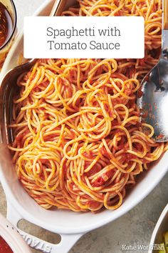 spaghetti with tomato sauce in a white bowl on a table next to spoons and condiments