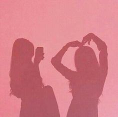 two women standing next to each other in front of a pink wall with the shadow of them