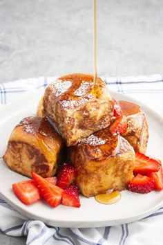 french toast with strawberries and syrup on a white plate, being drizzled with maple syrup