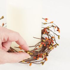 a person is holding a candle in front of a wreath with berries and leaves on it