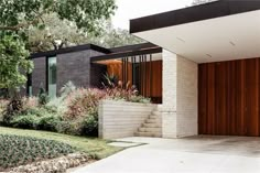 a modern house with wooden doors and brick walls, surrounded by greenery on both sides