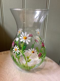 a glass vase with daisies painted on the outside and inside, sitting on a table