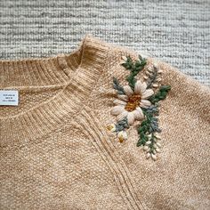 a sweater with flowers on it is sitting on the floor next to a tag that says,