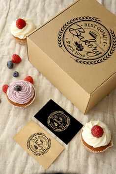 cupcakes with white frosting and raspberries are on a table next to the box