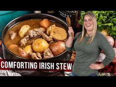 a woman standing in front of a pot full of stew with potatoes and carrots