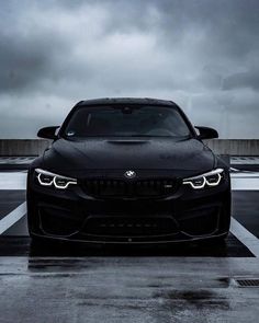 the front end of a black bmw car in a parking lot on a cloudy day