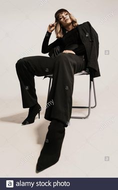 a woman sitting on a chair with her legs crossed, wearing high heeled boots - stock image